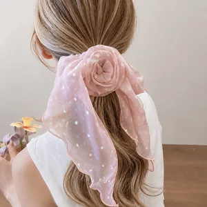 Chouchou élégant à ruban fleuri rose et pois blancs sur les cheveux du modèle.