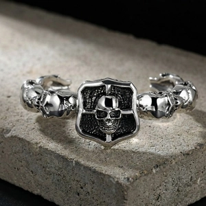 Close-up detail of a gothic silver skull bangle with shield and cross on a stone
