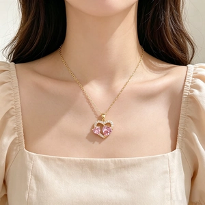 Nahaufnahme einer rosa Herz-Zirkonia-Halskette an einem Modell in einem beigen Kleid.