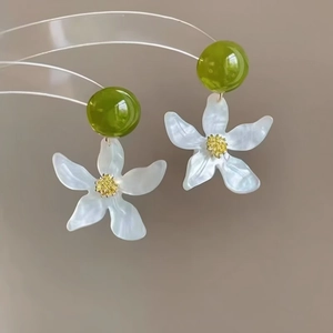 Close-up of white flower resin earrings with green beads and silver needles