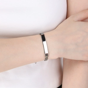 Detailopname van een zilveren Figaro-armband met een graveerbare ID-plaat om een pols.