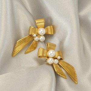 Detailed shot of golden ribbon bow earrings with pearls on a soft grey satin background