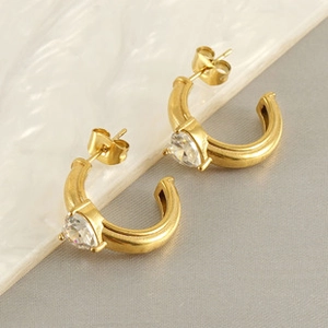 Detail of C-shaped gold-plated hoop earrings featuring a large clear heart-shaped zircon
