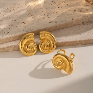 Macro shot of gold spiral sea shell stud earrings and open ring set on a stone surface