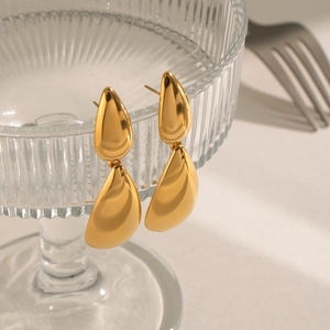 Polished gold stainless steel double teardrop earrings hanging on a textured glass bowl