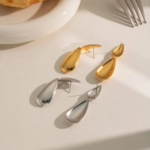 Polished gold and silver waterdrop earrings displayed on a ceramic tray with a dessert