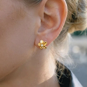 Elegant gold five-petal flower stud earring with sparkling crystal worn by a model