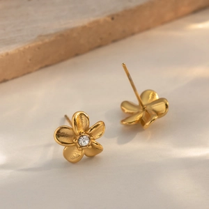 Elegant gold flower stud earrings with sparkling crystal center in a warm sunlight setting