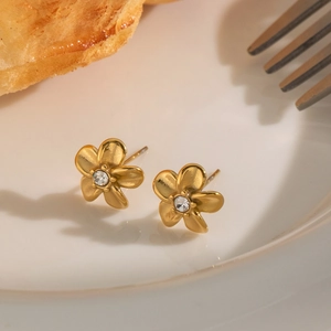 Macro detail of golden flower stud earrings with crystal center in a white ceramic dish