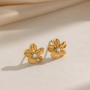 Close-up of golden flower stud earrings with sparkling crystal center on a white surface