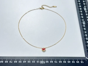 Elegante goldfarbene Halskette mit einem roten Herzanhänger auf einer Messskala
