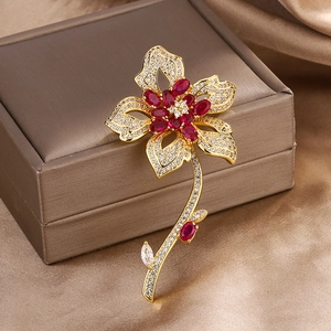 Elegant gold flower brooch with red gems and white crystals on a brown jewelry box