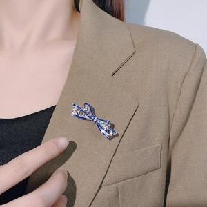 Elegant silver bow brooch with blue enamel and white crystals on a beige blazer
