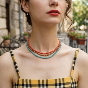 Detail of layered semi-precious bead necklaces with pearl earrings on a model