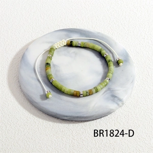 Detail van een handgeweven armband met groene natuursteen op een marmeren dienblad