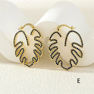 Makro-Detail von goldenen Creolen mit Blattdesign und Mikro-Pave blauen Zirkonia Steinen