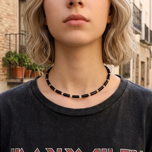 Handmade necklace with black cylinder beads and gold spacers on a female model outdoors