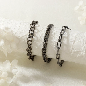 Dreiteiliges schwarzes Panzerketten-Armband-Set auf weißen zylindrischen Sockeln