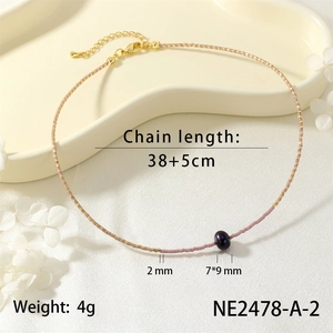 Detail shot of dainty beaded necklace with gold and pink seed beads and dark pearl pendant.