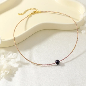 Delicate beaded necklace detail showcasing pink seed beads and a dark center pearl pendant.