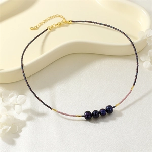 Detail shot of beaded clavicle chain featuring dark seed beads, purple rice beads, and pearls.