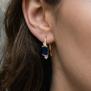Gros plan de boucles d'oreilles dorées avec pierre carrée bleue portées par un modèle