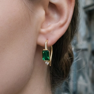 Gros plan de boucles d'oreilles émeraude en or avec des accents de diamants brillants