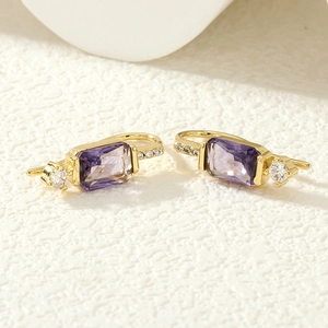 Vue détaillée de boucles d'oreilles dorées avec pierres violettes et diamants latéraux