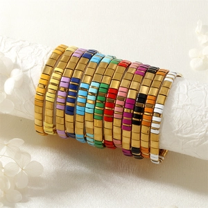 Gros plan de bracelets de perles Tila colorées empilés sur un support blanc texturé