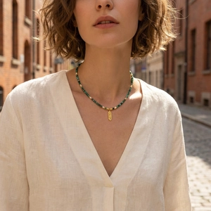 Detail of emerald green bead necklace with rectangular gold pendant on a model