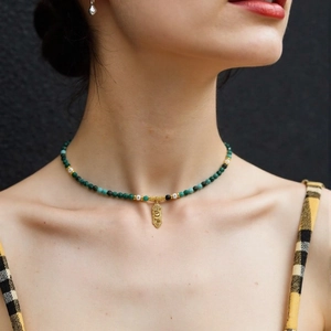 Macro shot of emerald gemstone necklace with gold snake pendant on model's neck