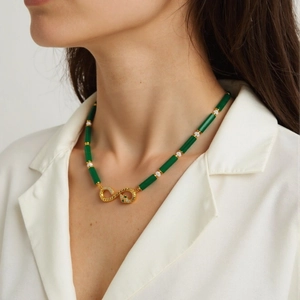 Close-up of emerald green beads and gold snake pendant necklace on model's neck