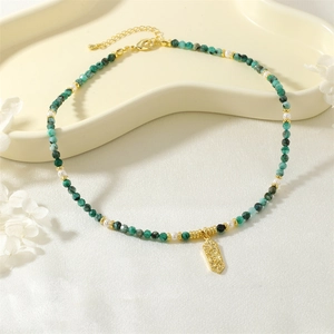 Macro detail of emerald beads and gold pendant necklace on ceramic display tray
