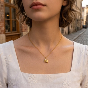 Collier minimaliste en or avec pendentif lettre M porté par un mannequin en ville