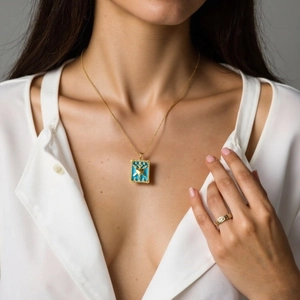 Detail of 18K gold-plated necklace with blue square pendant and heart motif on model
