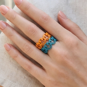 Detail of colorful smiley face rings in orange and cyan worn on hand