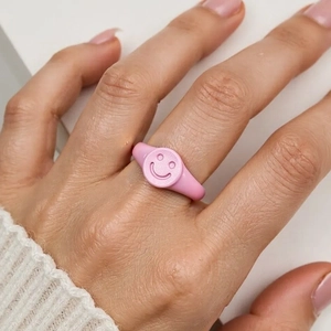 Macro shot of a pink macaron enamel ring with a heart smiley face on a finger