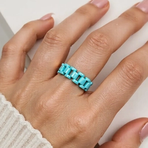 Detail of turquoise blue link ring on finger with polished ceramic finish texture