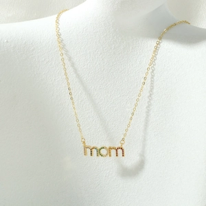 Detailopname van gouden MOM-hanger met gekleurde zirkoonstenen op een witte buste