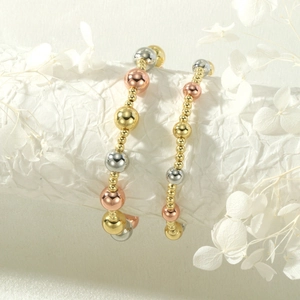 Detail of three-tone gold, silver and rose gold beaded elastic bracelets on a white pillar