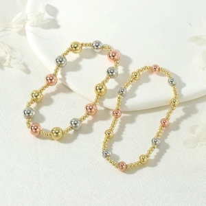 Detail of tri-color metal beaded bracelets in gold, silver, and rose gold on a white tray