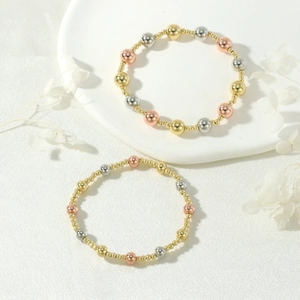 Detail of 18K gold-plated three-tone beaded elastic bracelets on white ceramic plate