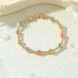 Detail of tri-color 18K gold plated beads on elastic bracelet with silk background