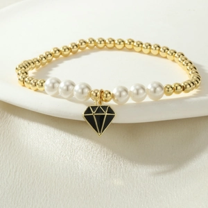 Detalle de pulsera de cuentas doradas y perlas blancas con colgante de diamante esmaltado