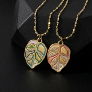 Detail of colorful enamel monstera leaf pendant with sparkling diamonds and gold chain