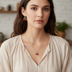 Detail of red cherry pendant necklace and earrings set with gold beaded chain and enamel leaf