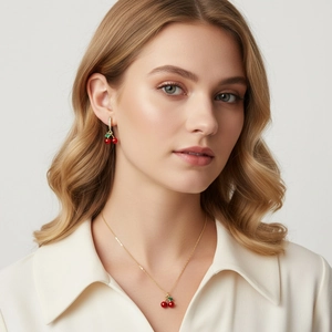 Close-up of red cherry pendant necklace and matching earrings worn by a model