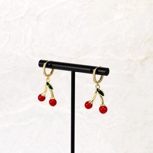 Detailed shot of red cherry drop earrings with green enamel leaves on a black T-stand
