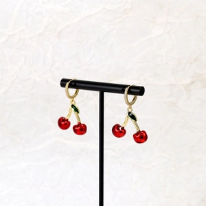 Close-up of red cherry earrings with green leaves and zircon-set gold hoops