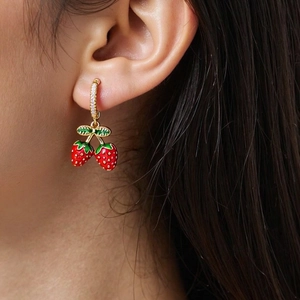 Detail of red strawberry earrings with green leaves and pavé crystals on a model's ear